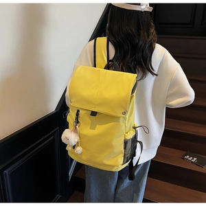 Detail of a bright yellow nylon backpack featuring a flap closure and white plush charm