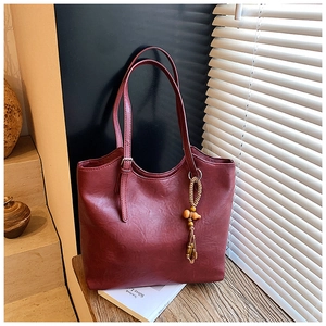 Detail of burgundy tote bag with leather texture and vintage gourd tassel pendant