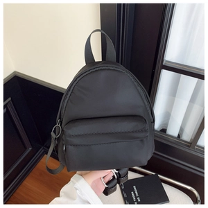 Detail of black nylon mini backpack featuring a front zipper pocket and adjustable straps