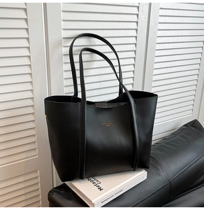 Dettaglio della borsa tote nera con logo dorato su superficie in pelle opaca liscia