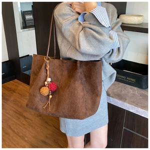 Detail of dark brown faux suede tote bag with decorative plush pom-pom pendant charm