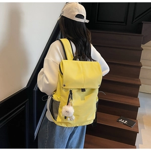 Detail of a bright yellow nylon backpack featuring a white plush charm and side mesh pocket