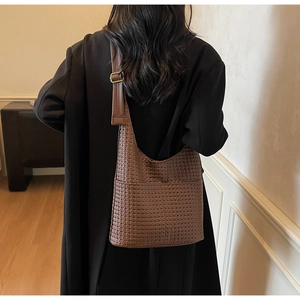 Détail du sac cabas tressé marron foncé sur un manteau noir avec vue sur la texture et bandoulière