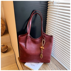 Close-up of wine red tote bag featuring vintage bead tassel and adjustable shoulder straps