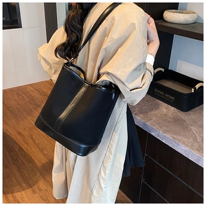 Classic black leather bucket bag with adjustable strap shown on model in warm interior