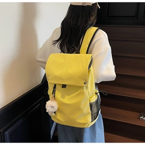 Detail of waterproof nylon backpack in bright yellow with cute plush pendant on stairs
