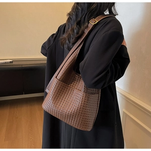 Détail d'un sac seau en cuir tressé marron avec texture riche et bandoulière large