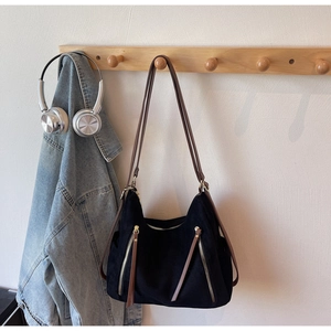 Detailed view of a black canvas hobo bag with brown leather strap and gold zipper accents