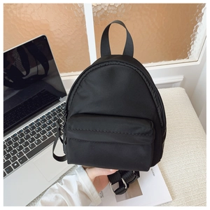 Mini black nylon backpack held by hand in a modern office desk and laptop setting