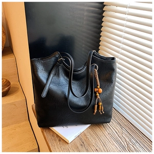 Close-up of a black leather tote bag with wooden bead tassel on a wooden table