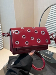 Deep red patent leather crossbody bag with silver eyelets and accordion pleats