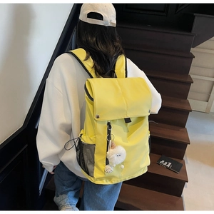 Detailed view of yellow nylon backpack featuring side mesh pocket and plush ball charm