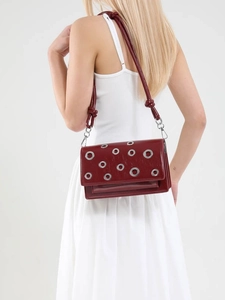 Crossbody wine red leather bag with metal eyelets worn by a model against white