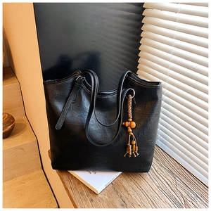Detail view of black tote bag with wooden bead charm and adjustable handle buckle
