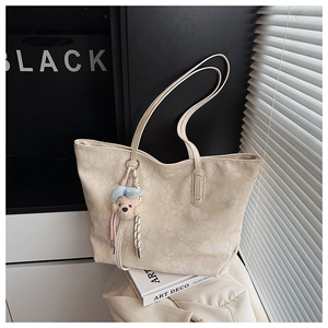 Detail einer beigen Jacquard-Tasche mit Blumenmuster und süßem Bärenanhänger auf Buch