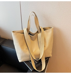 Detail of beige canvas tote bag with double straps and striped lining on leather sofa