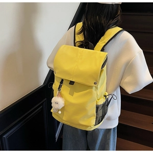 Detail of bright yellow nylon backpack with white plush pendant on wooden stairs