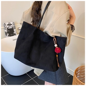 Detail of a black underarm tote bag with a red pompom and tassel pendant decoration