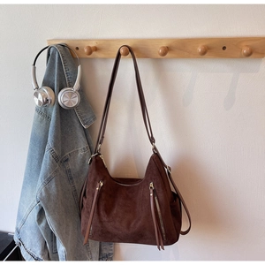 Detail of dark brown matte suede shoulder bag with dual vertical zippers on wooden hook