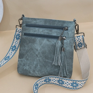 Detail view of a vintage crossbody bag with dual tassel zippers and embroidered strap