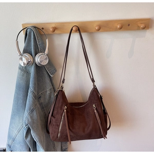 Close-up of brown suede shoulder bag with long leather tassels and decorative zippers
