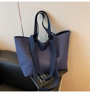 Detail of dark blue denim tote bag with dual straps on a leather sofa surface