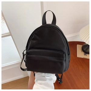 Detail of a minimalist black mini backpack with smooth nylon texture and zipper pockets