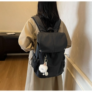 Close-up of black nylon backpack featuring a flap cover, metal buckle and plush pendant