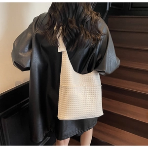 Détail du sac seau hobo blanc tressé avec poche extérieure sur une veste en cuir
