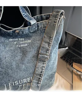 Detail of adjustable denim shoulder strap and metal buckle on blue washed tote bag