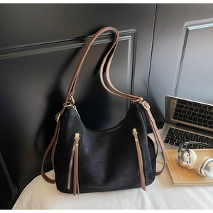 Detail of black suede tote bag with brown leather straps and gold zippers on a desk