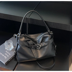 Detail of black pebbled leather tote bag with silver buckle and design book background