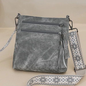 Detail view of grey crossbody bag featuring multi-zipper layers and embroidered wide strap