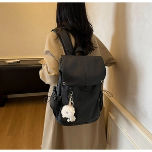 Detail of a black nylon backpack featuring a silver snap button and white plush charm