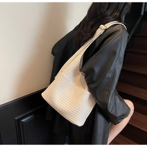 Détail d'un sac seau tressé blanc avec bandoulière réglable porté sur un blouson en cuir