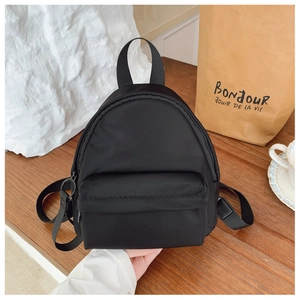 Close-up of a mini black nylon backpack held by a hand to showcase its compact travel size