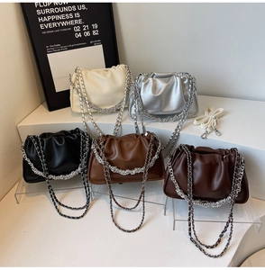 Five pleated cloud bags in neutral colors with chain straps displayed on white podiums