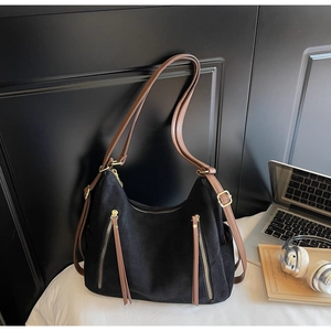 Detail of matte black tote bag featuring brown faux leather straps and dual gold zippers