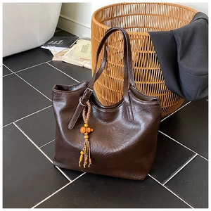 Detail of dark brown faux leather tote bag with wooden bead tassel and metal buckle strap