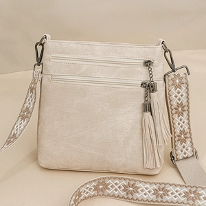 Close-up of beige crossbody bag featuring dual zippers with tassels and jacquard strap