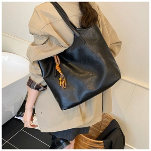 Detail of black leather tote bag with ethnic wooden beads and tassel on a model