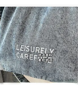 Macro shot of light blue denim fabric with white 'LEISURELY CAREFREE' printed lettering