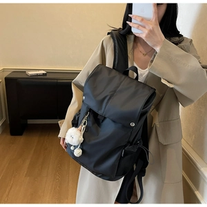 Detail of black waterproof nylon backpack featuring a large flap and cute plush charm