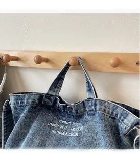 Detail of blue denim tote bag featuring sturdy handles and white casual typography print