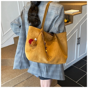 Detail of a large mustard yellow suede tote bag featuring a decorative pompom tassel