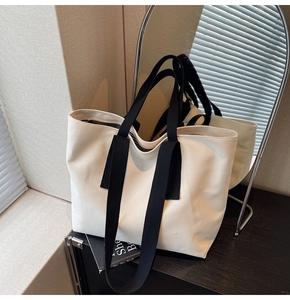 Detail of off-white canvas tote bag featuring black woven straps and durable fabric texture