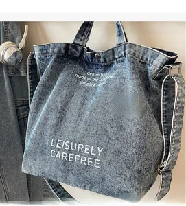 Detail of blue washed denim tote bag with artistic white lettering and adjustable strap