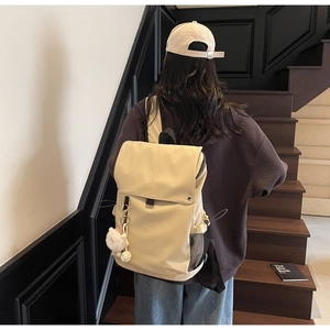 Detail of cream nylon backpack featuring a cute plush pendant and mesh side pocket