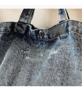 Close-up of light blue denim tote with metal magnetic clasp and artful text print