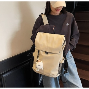 Detail view of a beige nylon backpack featuring side mesh pockets and a plush doll charm